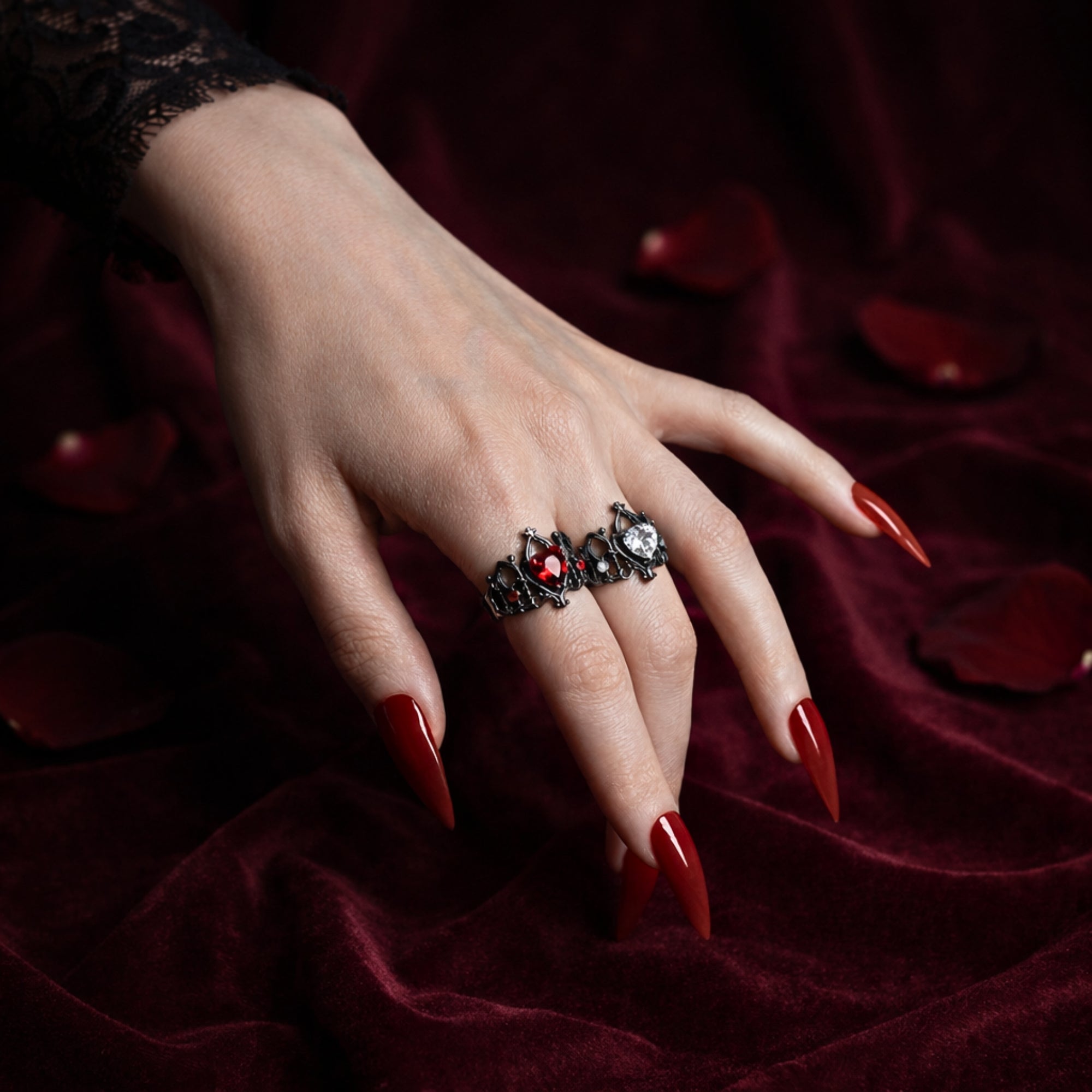 Devotion gothic ring with red heart stone worn on hand against burgundy velvet with rose petals